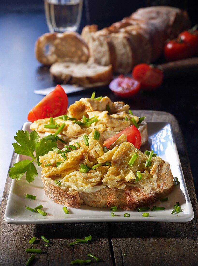 Two slices of baguette topped with scrambled egg and tomatoes