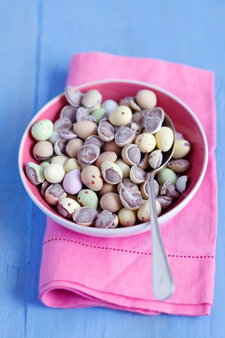 A bowl of chocolate eggs on a pink cloth
