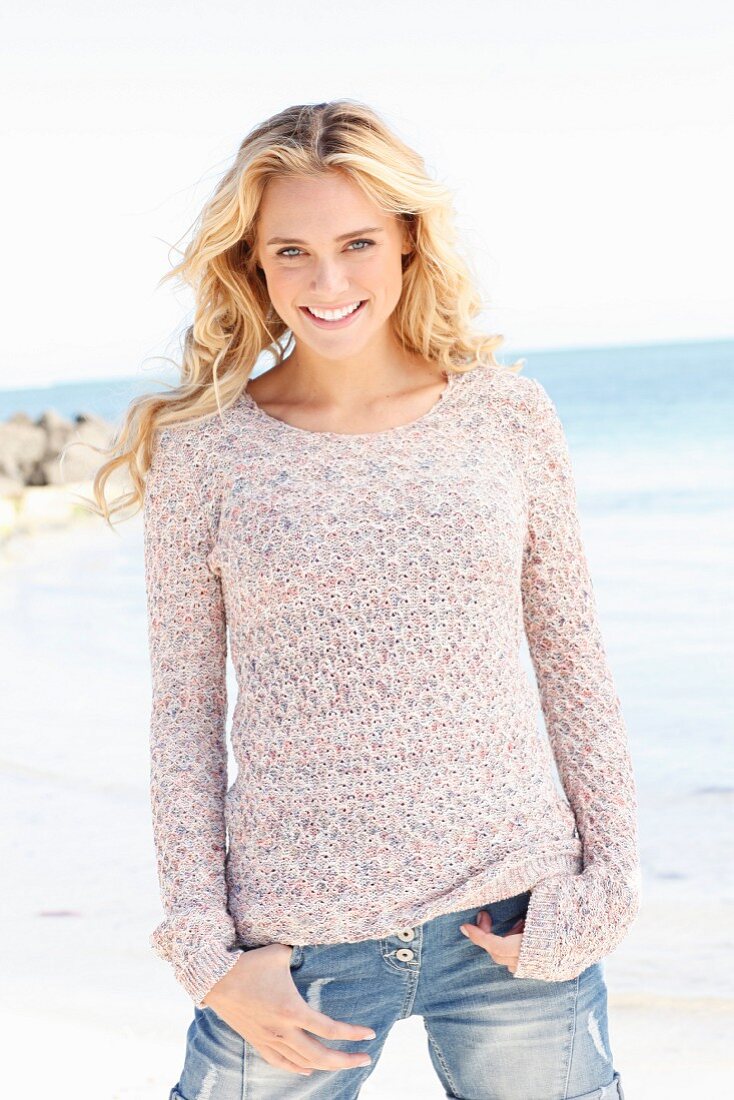 A young blonde woman wearing a knitted jumper and jeans by the sea