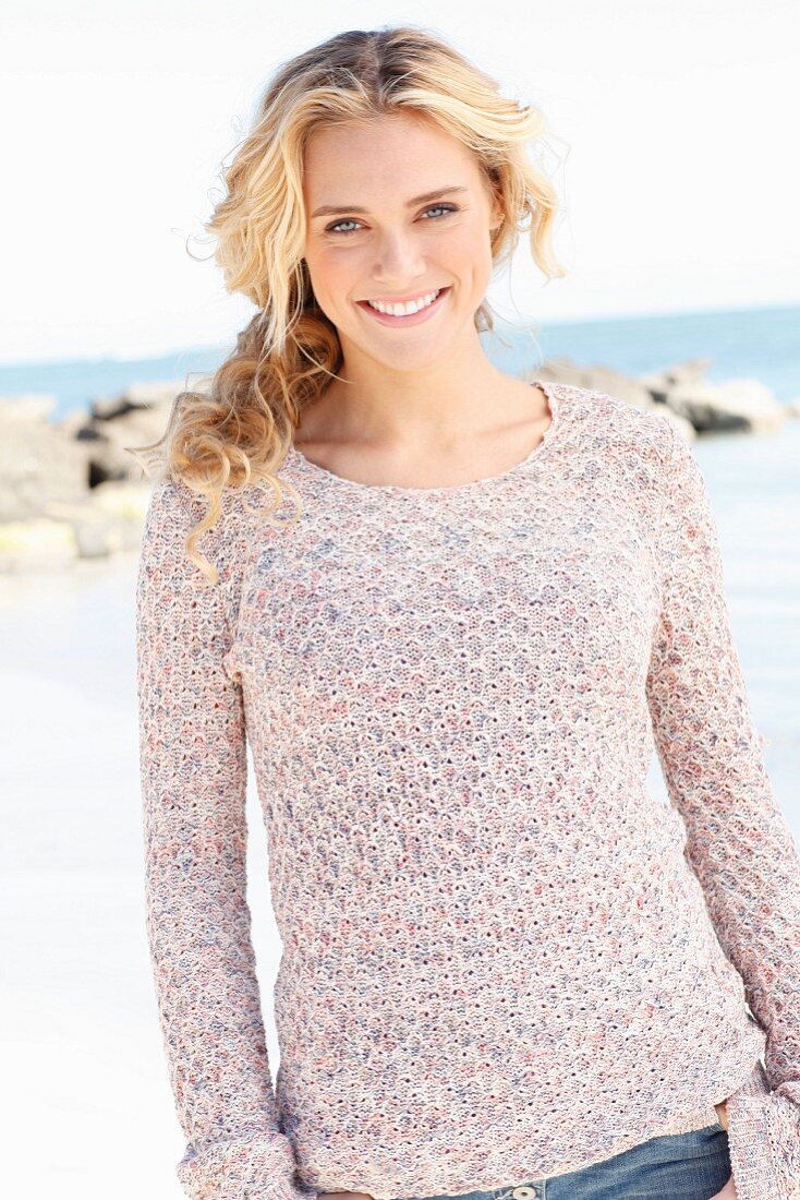 A young blonde woman by the sea wearing a knitted jumper
