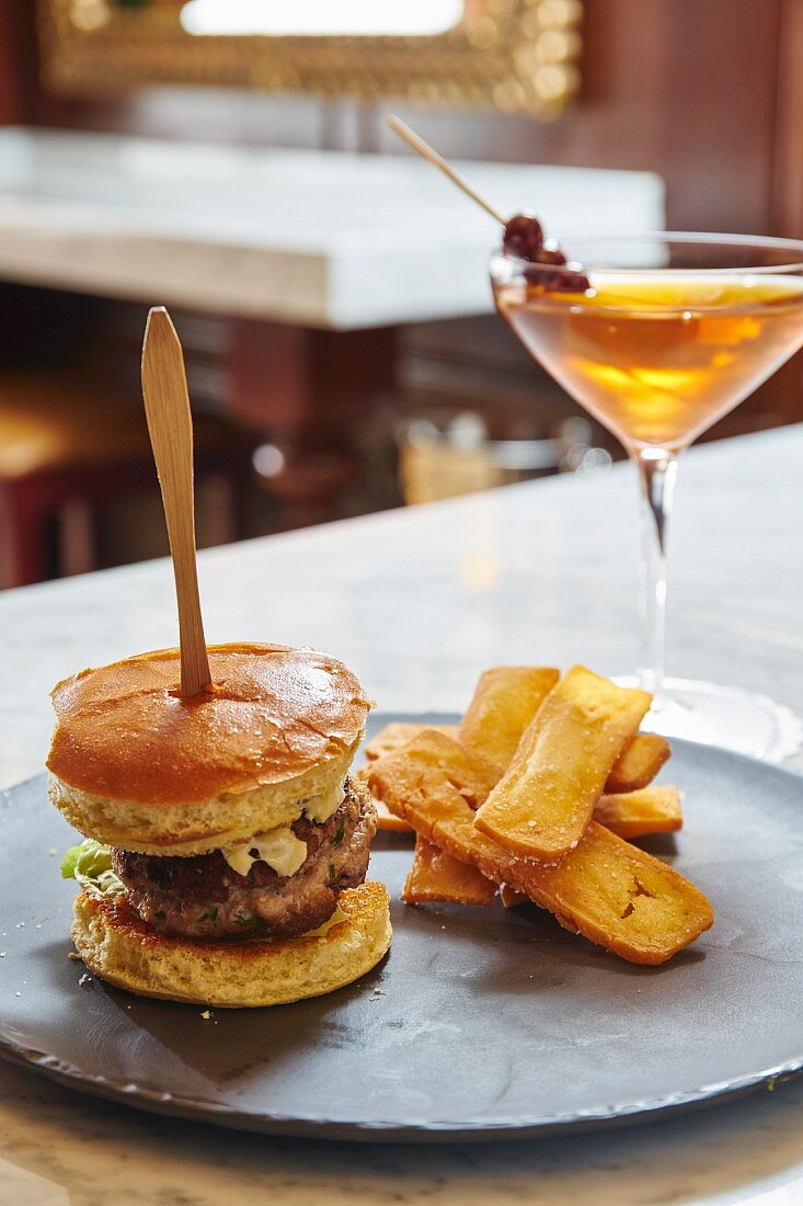 A cheeseburger and potato wedges with a Martini in a restaurant