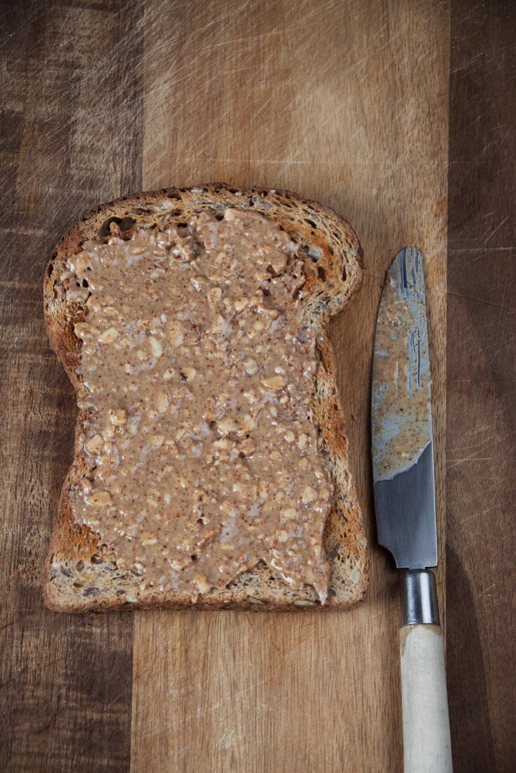 Wholemeal toast with peanut butter spread on a chopping board with a knife