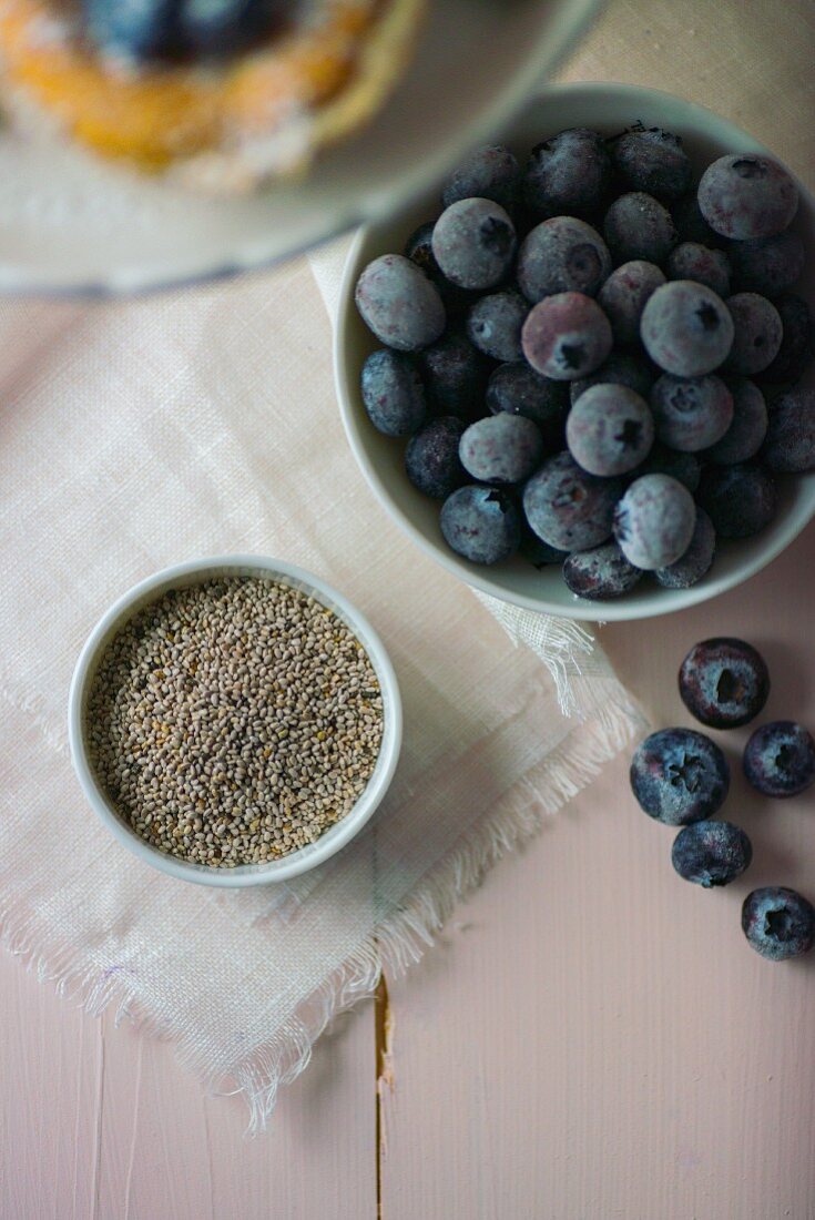 Chia seeds in a white bowl next to blueberries