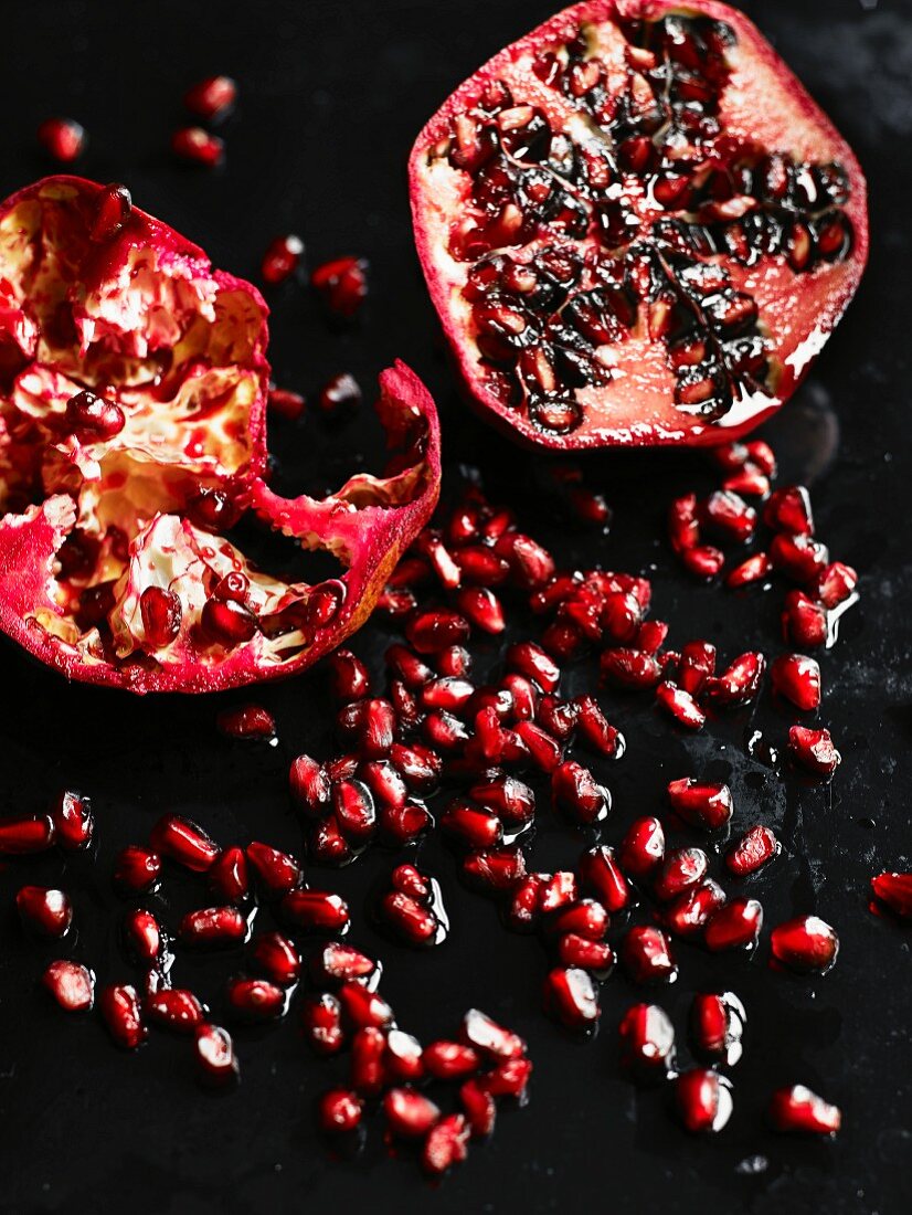 A halved pomegranate and pomegranate seeds on a wooden surface