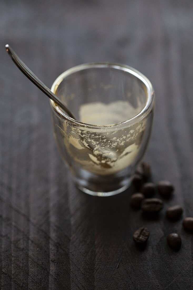 An empty espresso glass with a spoon on a wooden surface