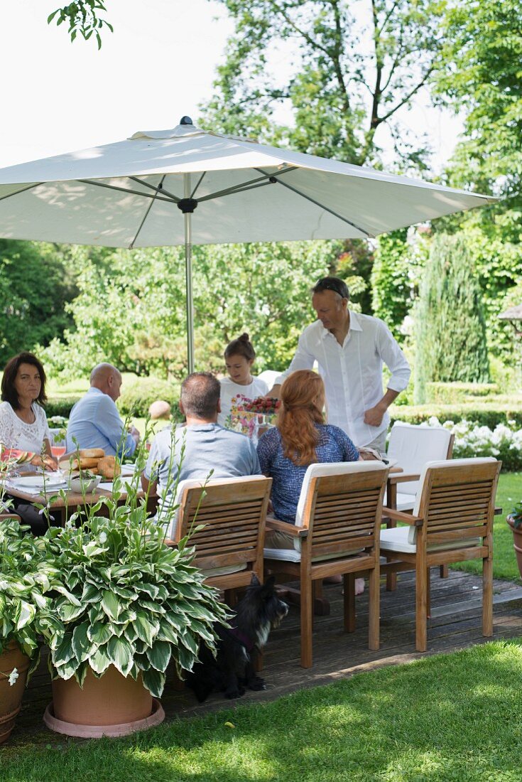 Gäste an gedecktem Tisch mit Sonnenschirm im Garten