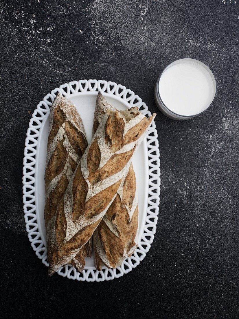 Drei Sauerteig-Baguettebrote auf Porzellanteller daneben ein Glas Milch