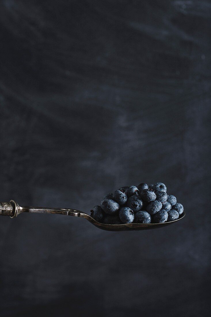Blueberries on spoon on a dark surface