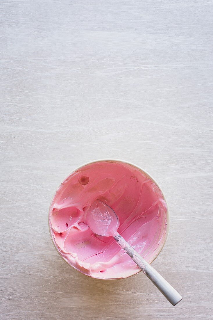 Pink buttercream in a bowl with a spoon