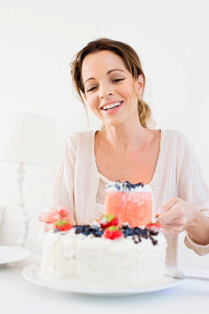 A woman taking a slice of berry cream cake