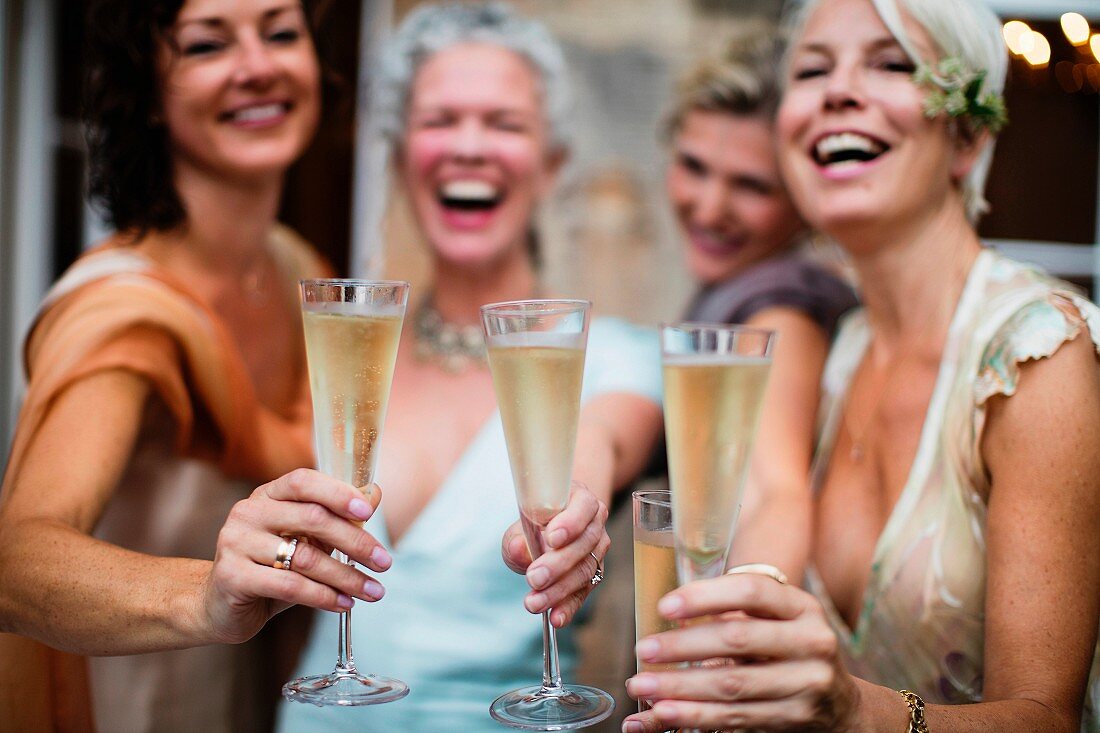 Four women wearing evening dresses toasting with champagne