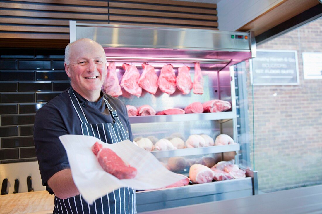 A butcher holding a raw steak in butcher's shop