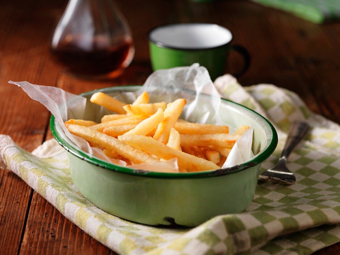 French fries in an enamel bowl on a tea towel with a bottle of vinegar