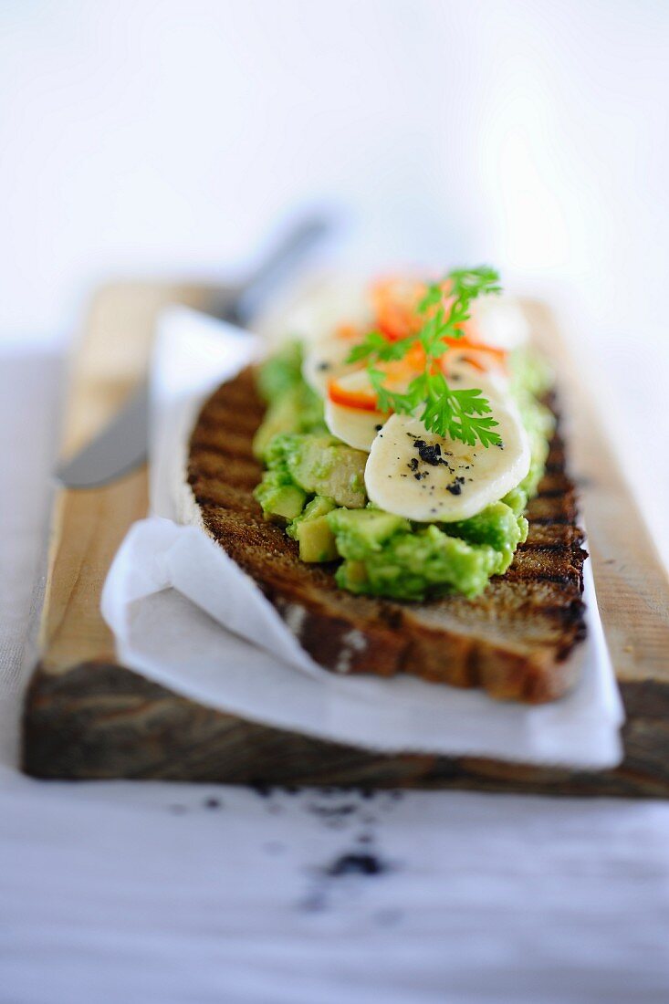 A slice of grilled bread topped with avocado cream and bananas