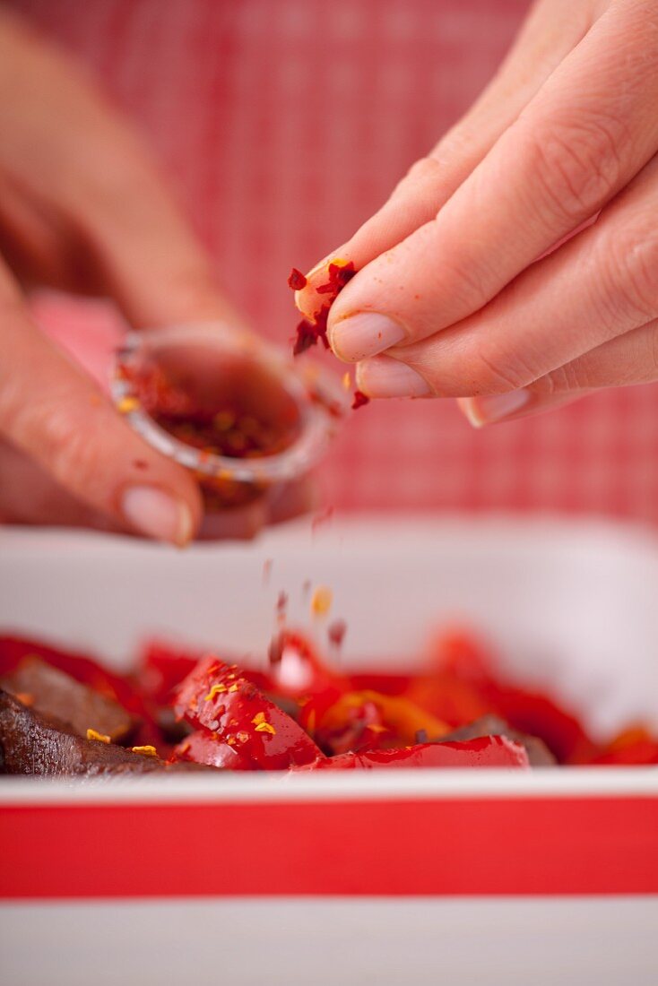 Chilli flakes being sprinkled over beef with peppers