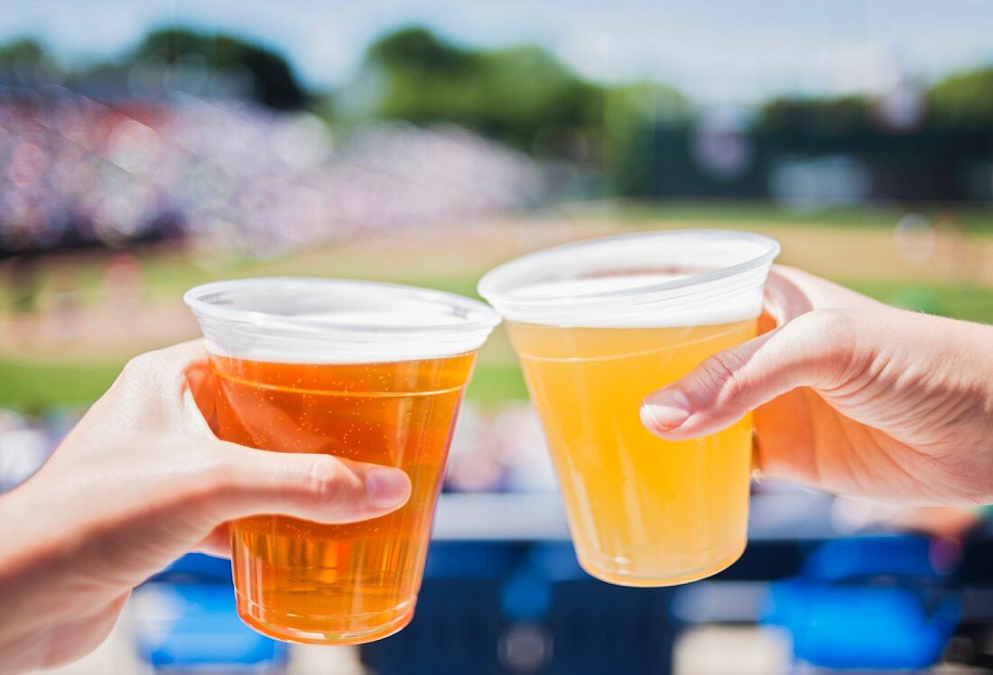Hands raising a toast with beer in plastic cups
