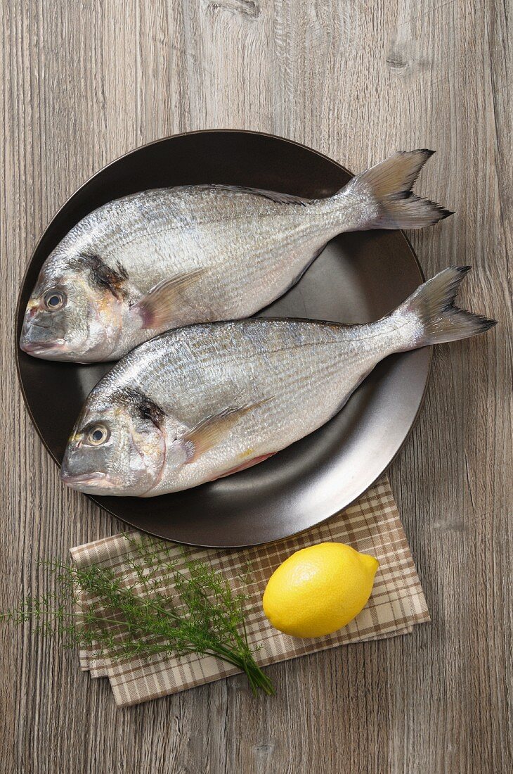Two sea bream on a plate with lemon and dill