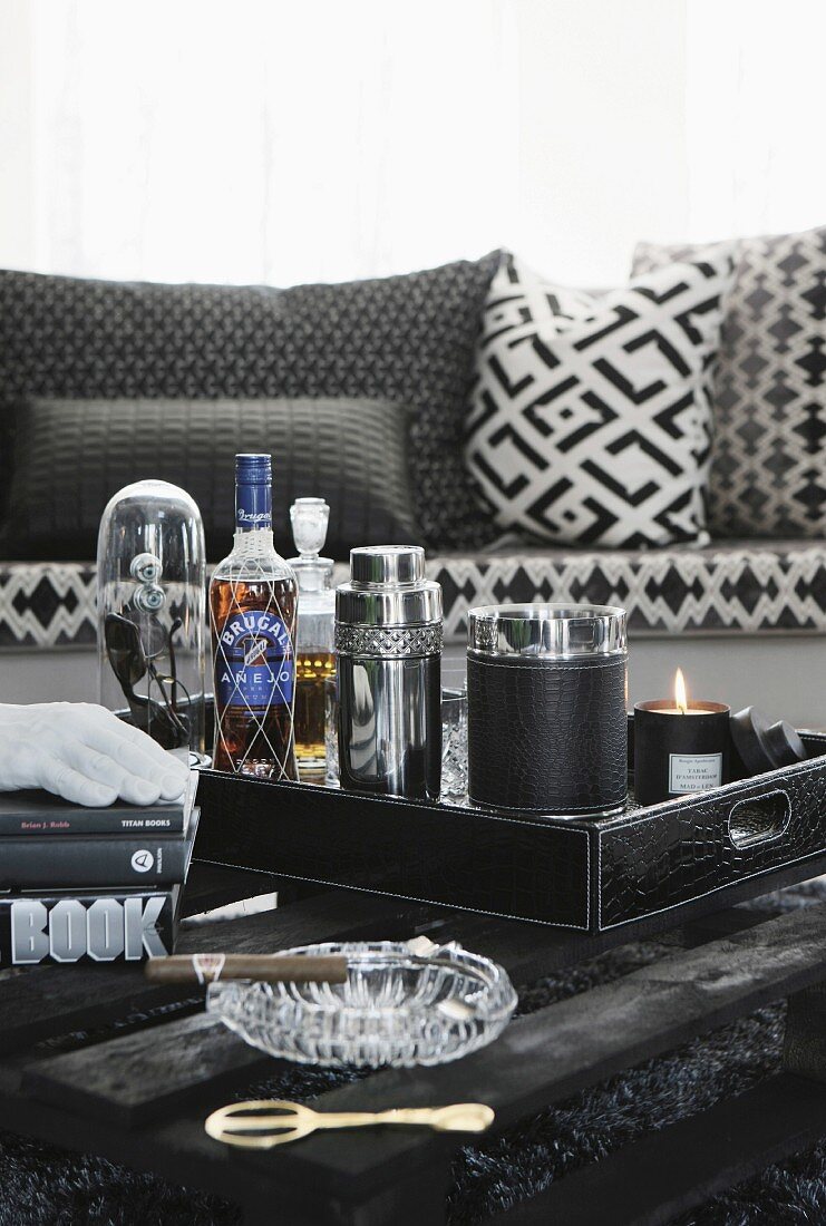 Minibar with cocktail shaker on tray and cigar in ashtray on black table made from pallet in front of sofa