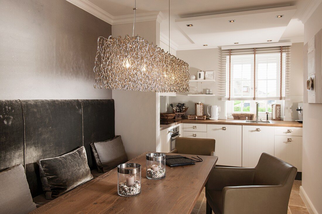 Built-in bench with upholstered backrest and brown leather armchair around wooden table below pendant lamp