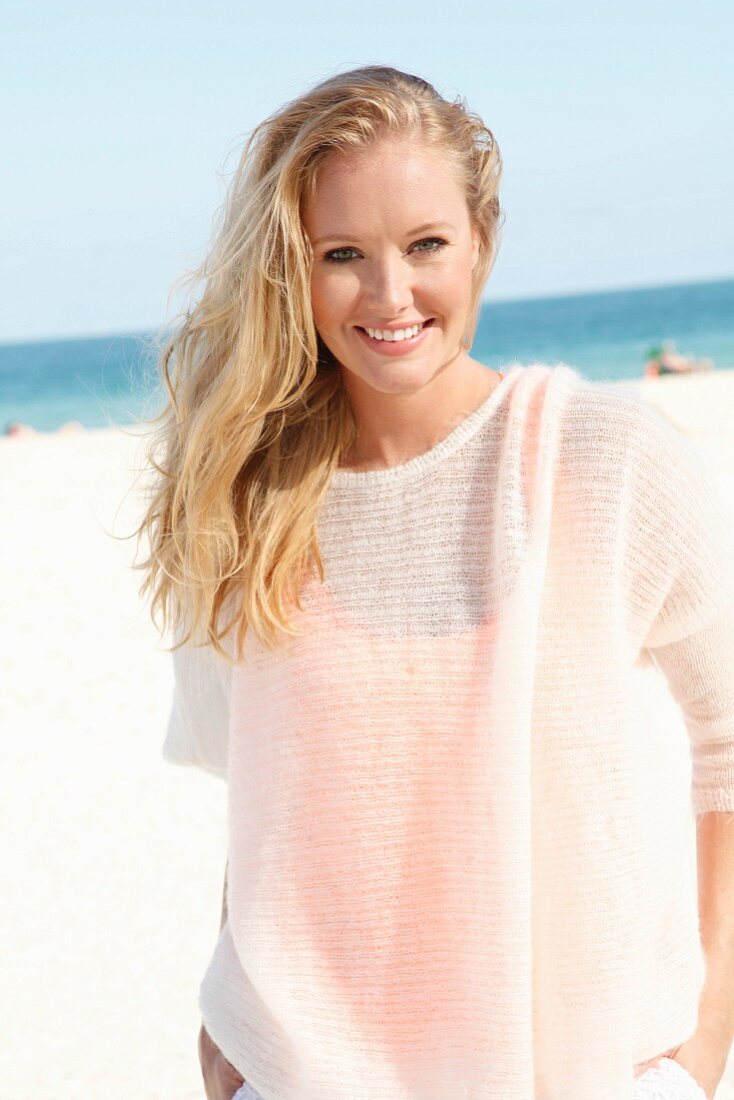 Blonde Frau in durchsichtigem Wollpulli am Strand