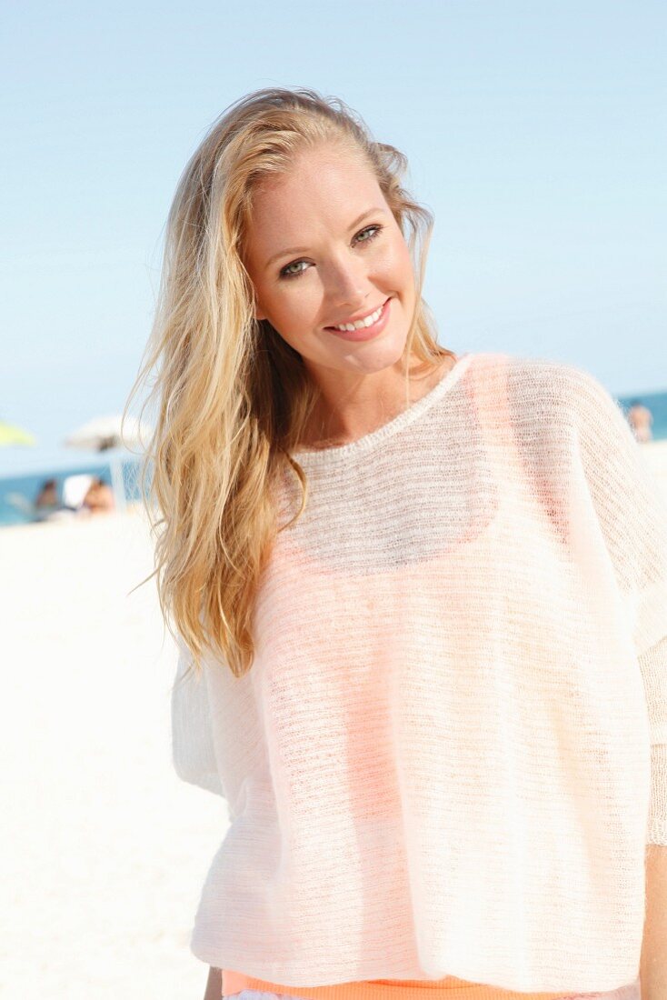 A blonde woman on the beach wearing a see-through woollen jumper