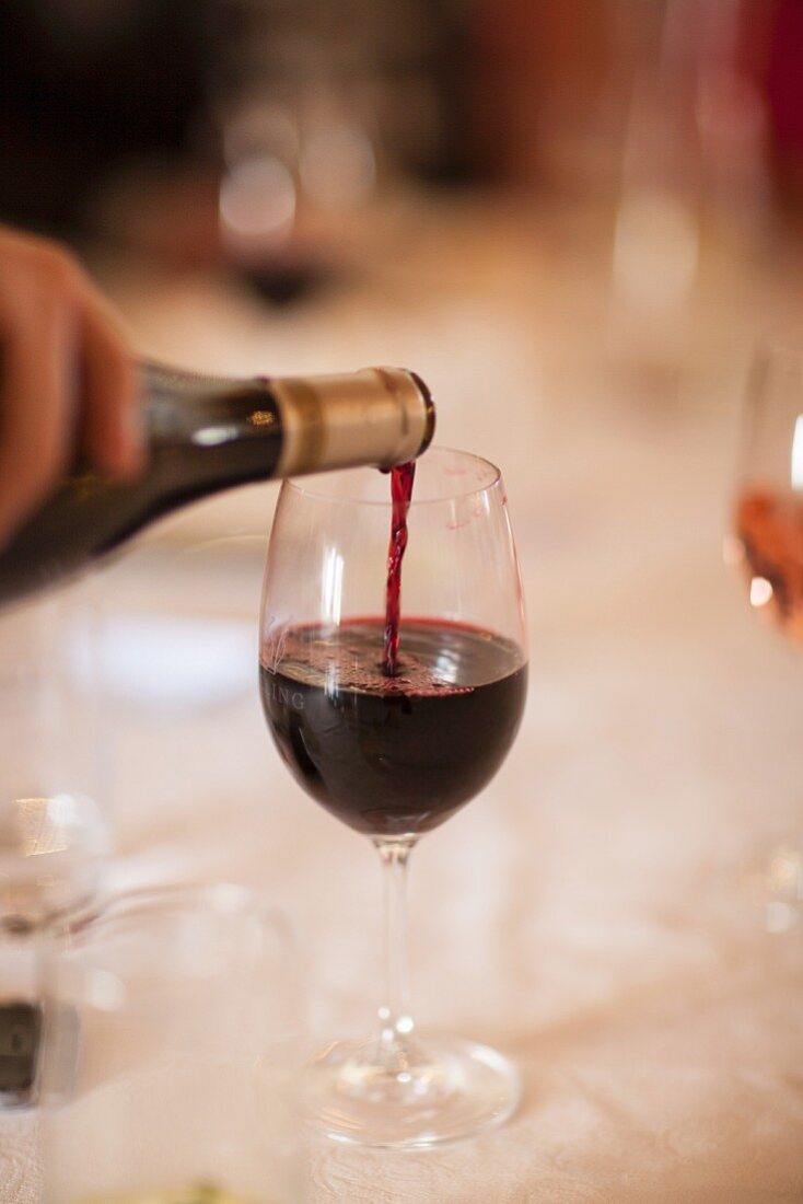 Rotwein wird aus Flasche in Weinglas gegossen