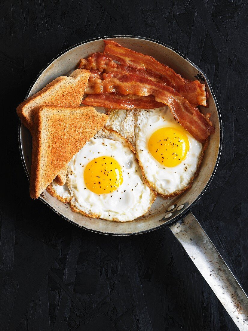 Fried eggs with bacon and toast in a pan
