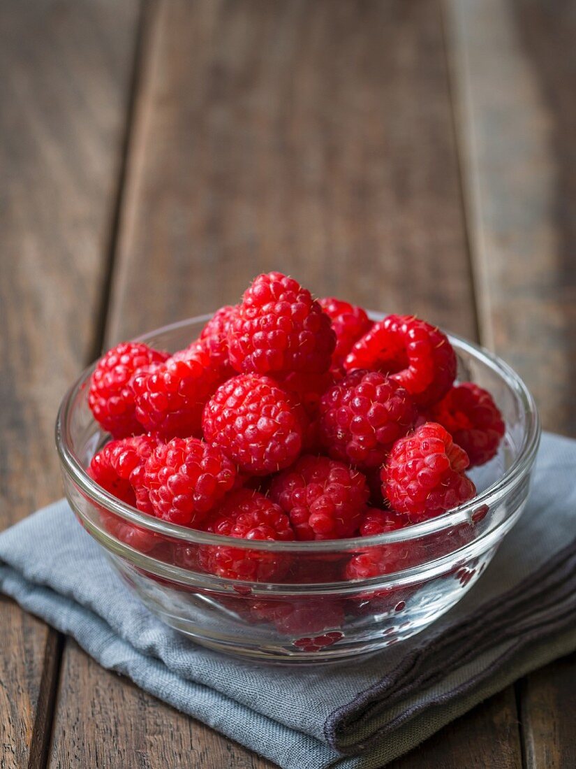 Fresh raspberries in a glass bowl on a wooden surface
