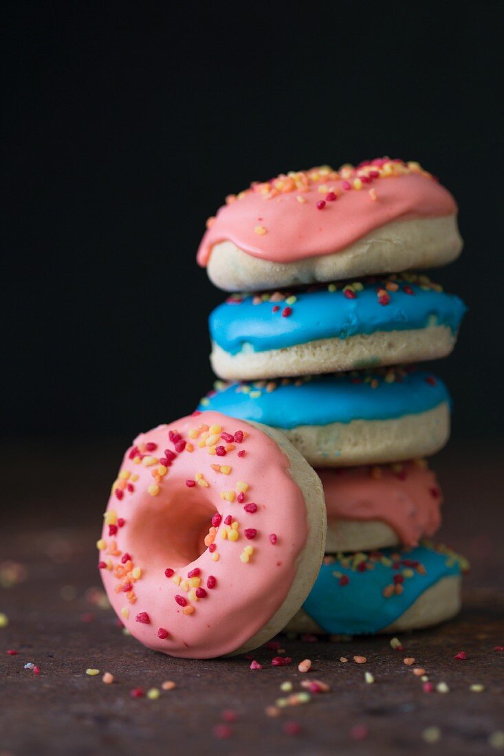 A stack of doughnuts with blue and pink icing and sugar sprinkles