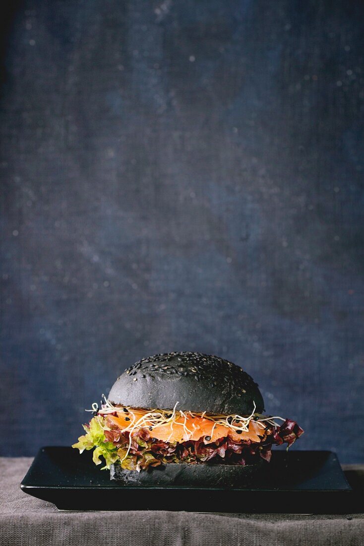 Homemade black burger with salmon, sprouts and lettuce