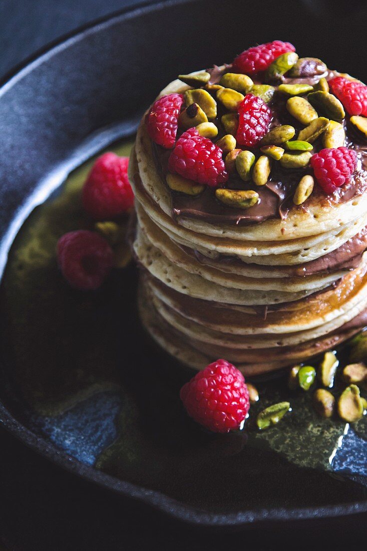 A stack of pancakes with chocolate cream, pistachio nuts and raspberries