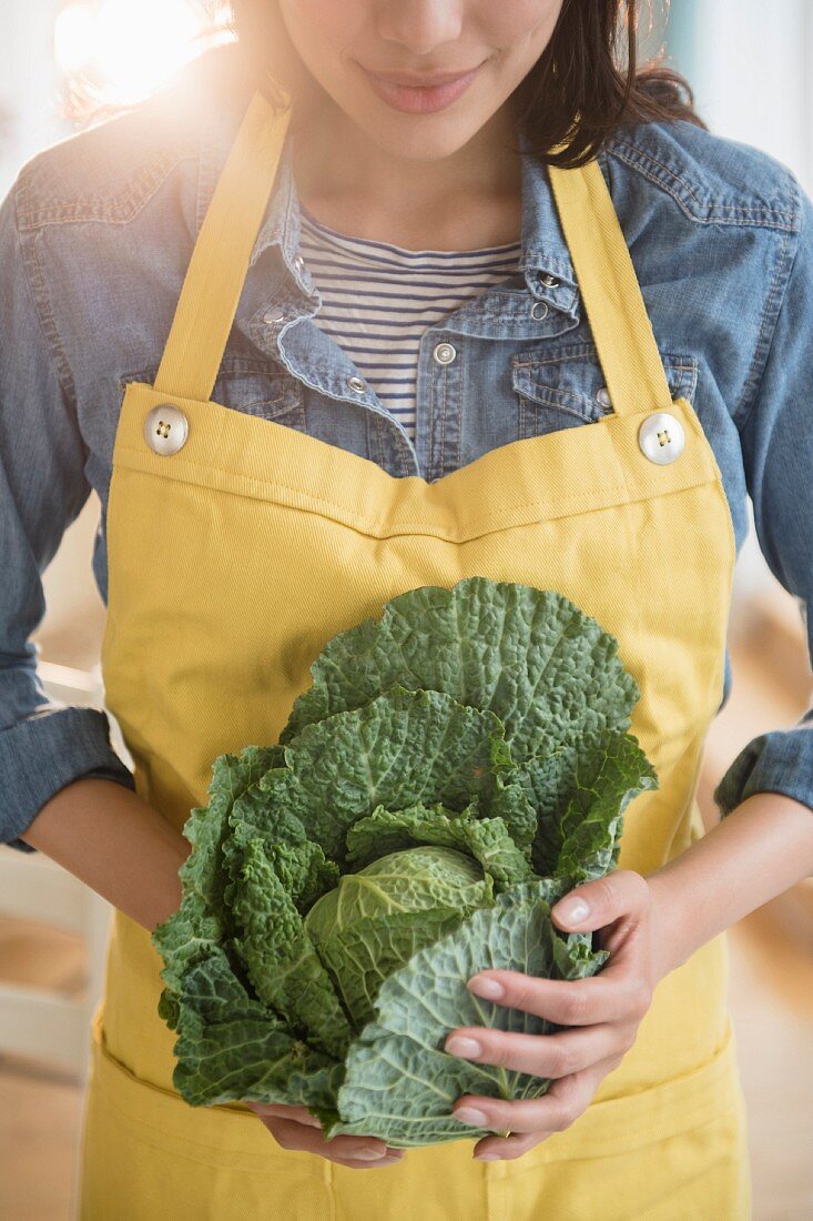 A young woman holding a whole savoy cabbage
