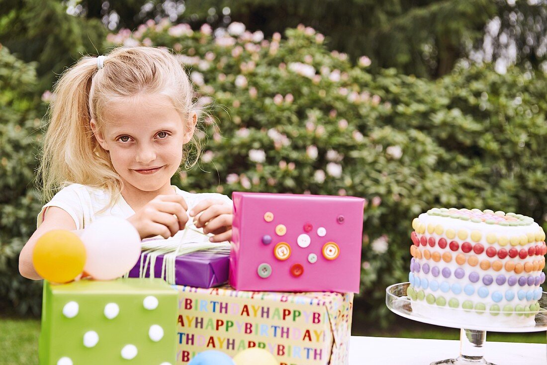 A blonde girl with birthday presents and a cake in a garden