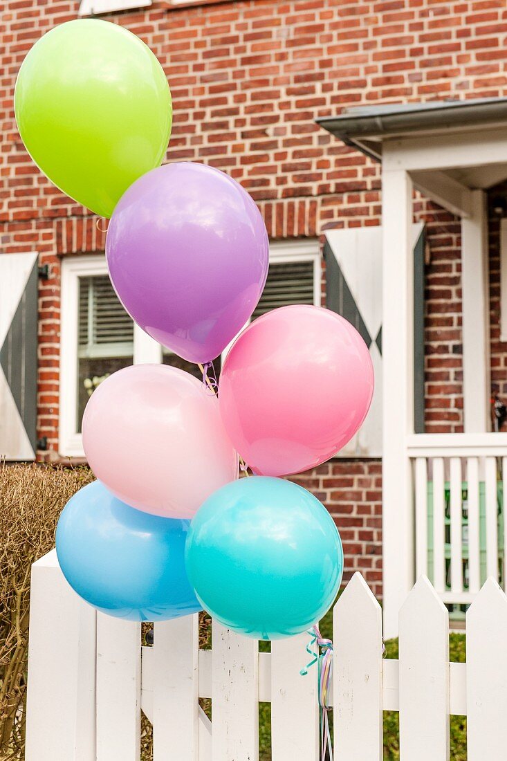 Colourful balloons tied to white garden gate