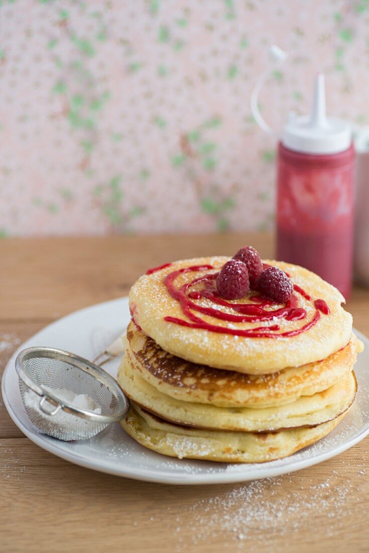 A stack of pancakes with raspberries and icing sugar