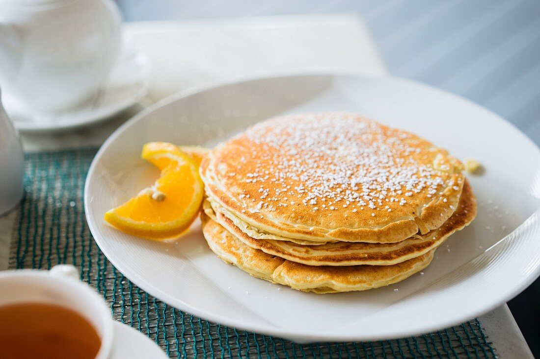 Gestapelte Pancakes mit Puderzucker und Orangenschnitz
