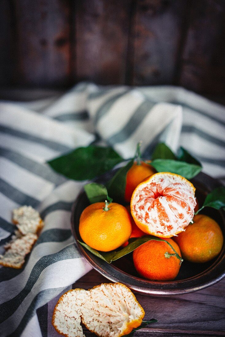 Mandarins with leaves in a metal bowl on a rustic wooden surface