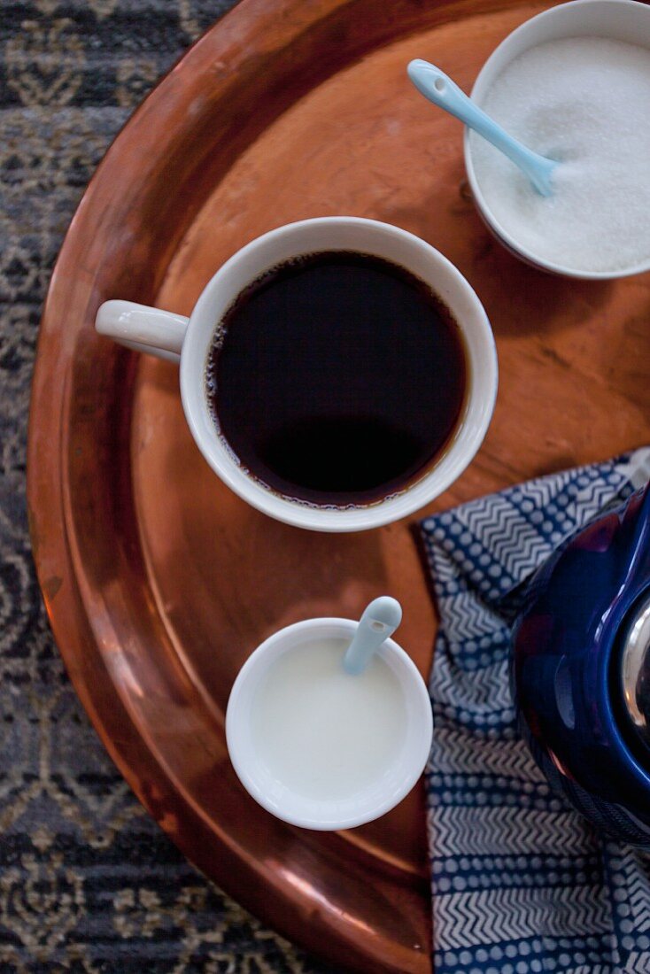 Eine Tasse Kaffee mit Milch und Zucker auf Kupfertablett (Aufsicht)