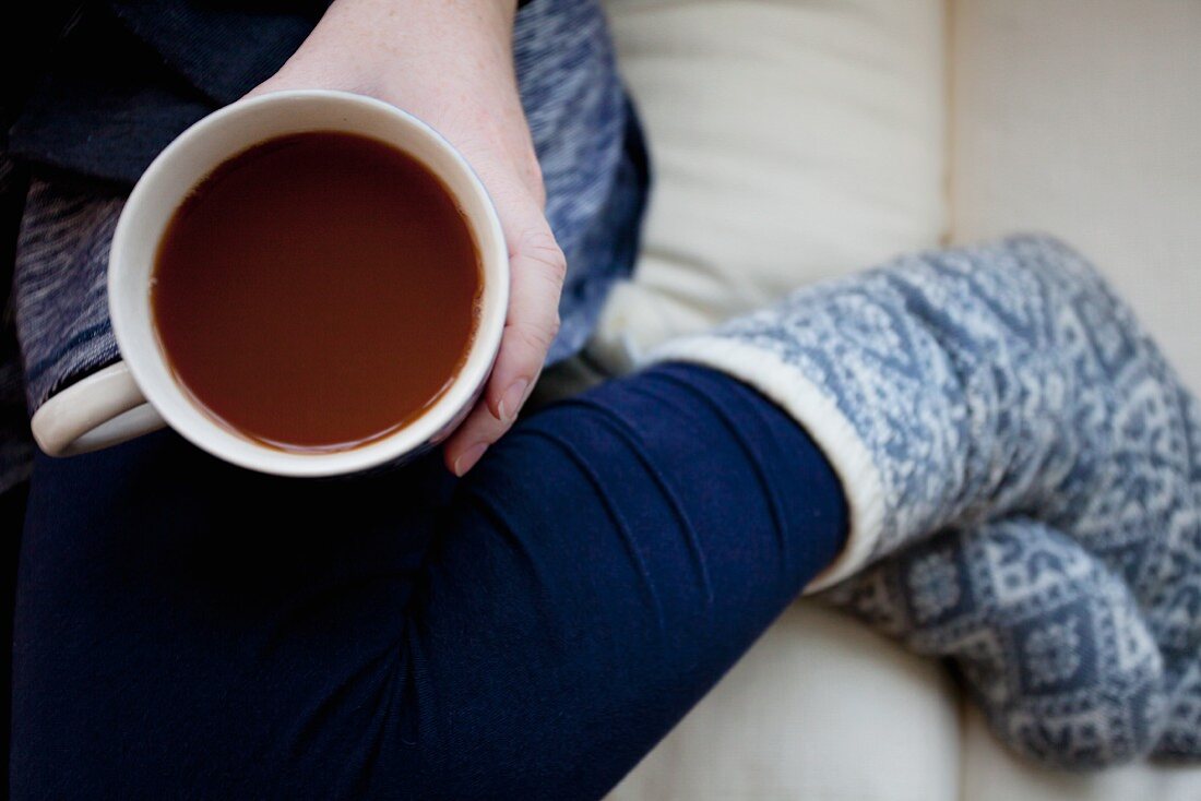 Frau mit Tasse Kaffee und Wintersocken auf Sofa sitzend