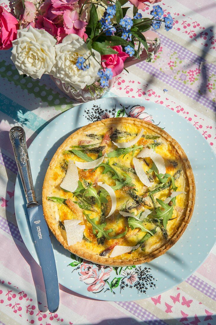 Quiche with green asparagus, ham and rocket on a table outside