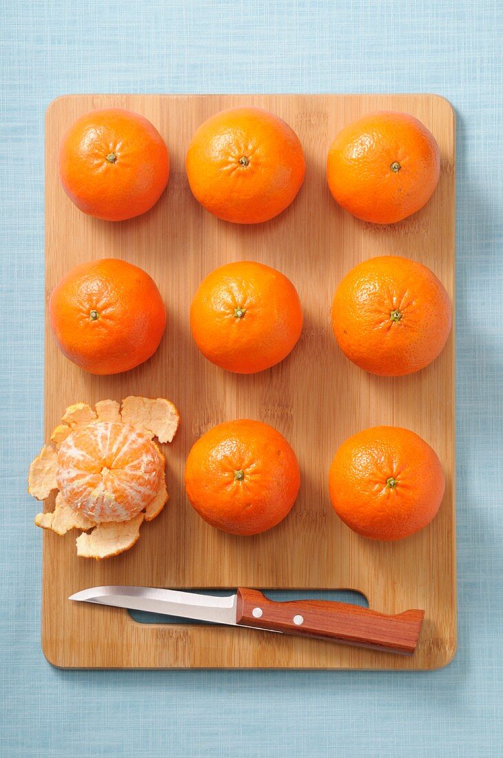 Whole mandarins and a peeled mandarin on a wooden board
