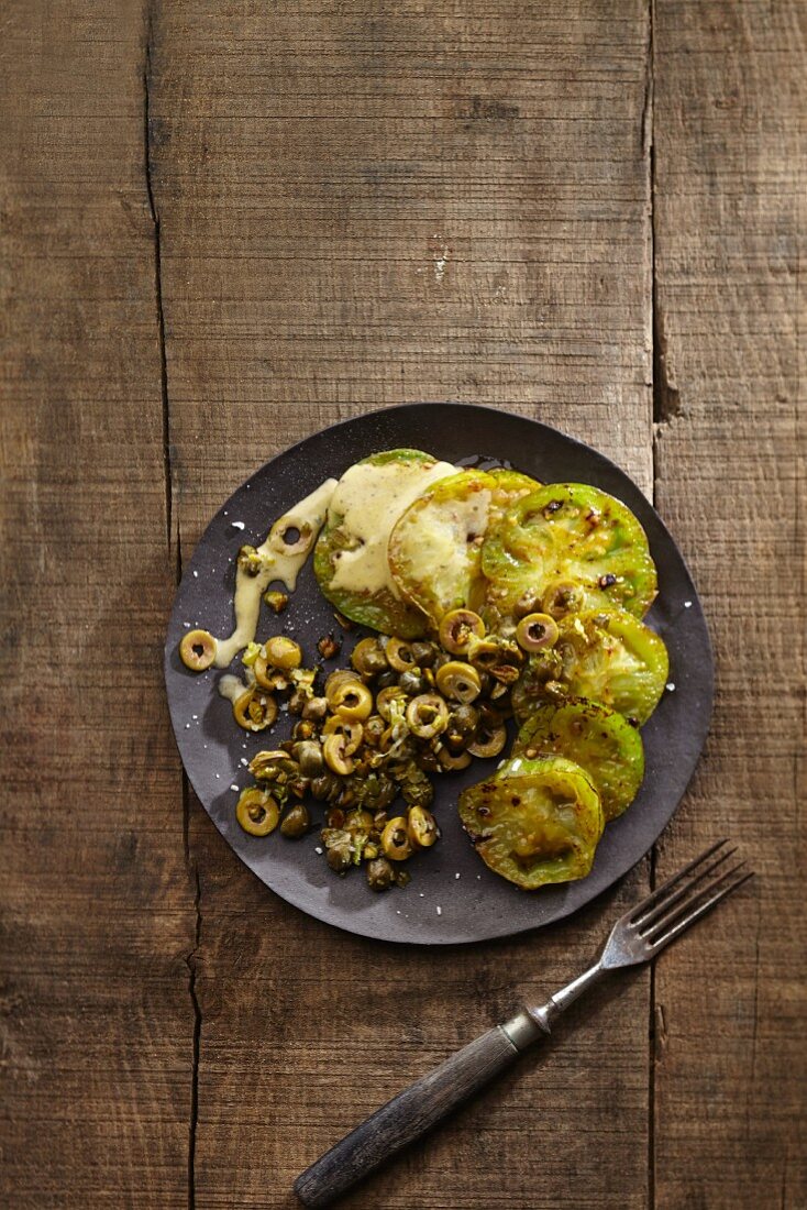 A salad of fried green tomatoes with green olives, caper flowers and pistachios