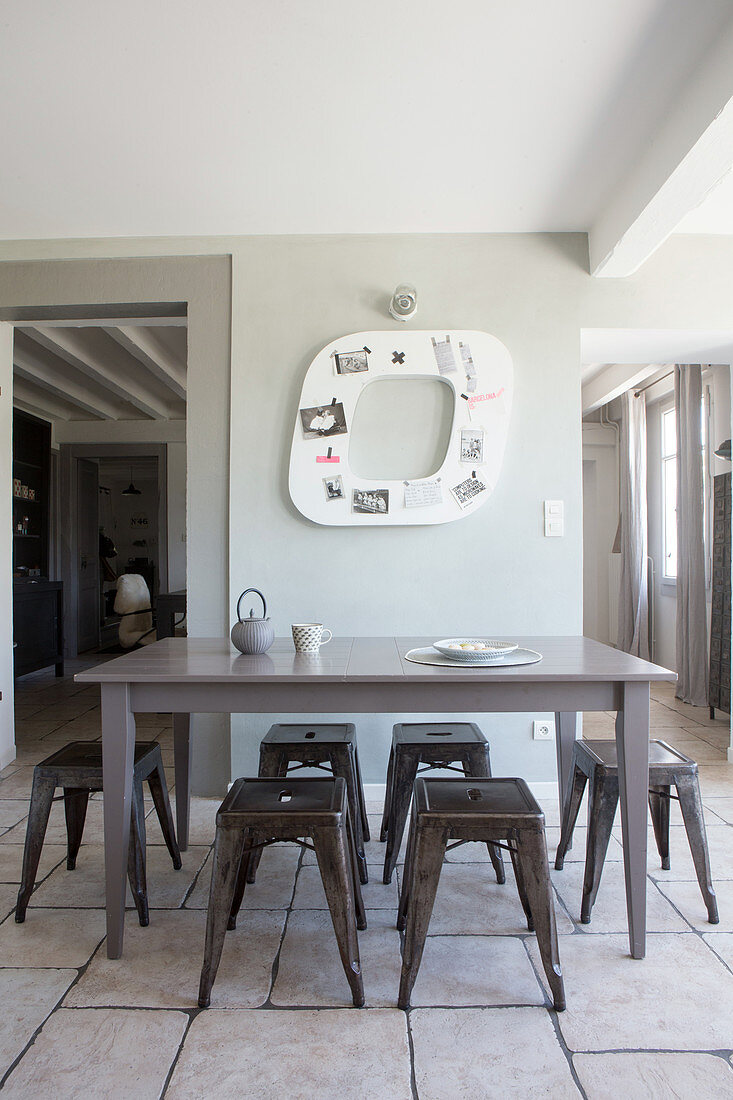 Klassiker Metallhocker um grauen Holztisch vor Wanddekoration und Durchgängen, heller Fliesenboden in restauriertem Altbau