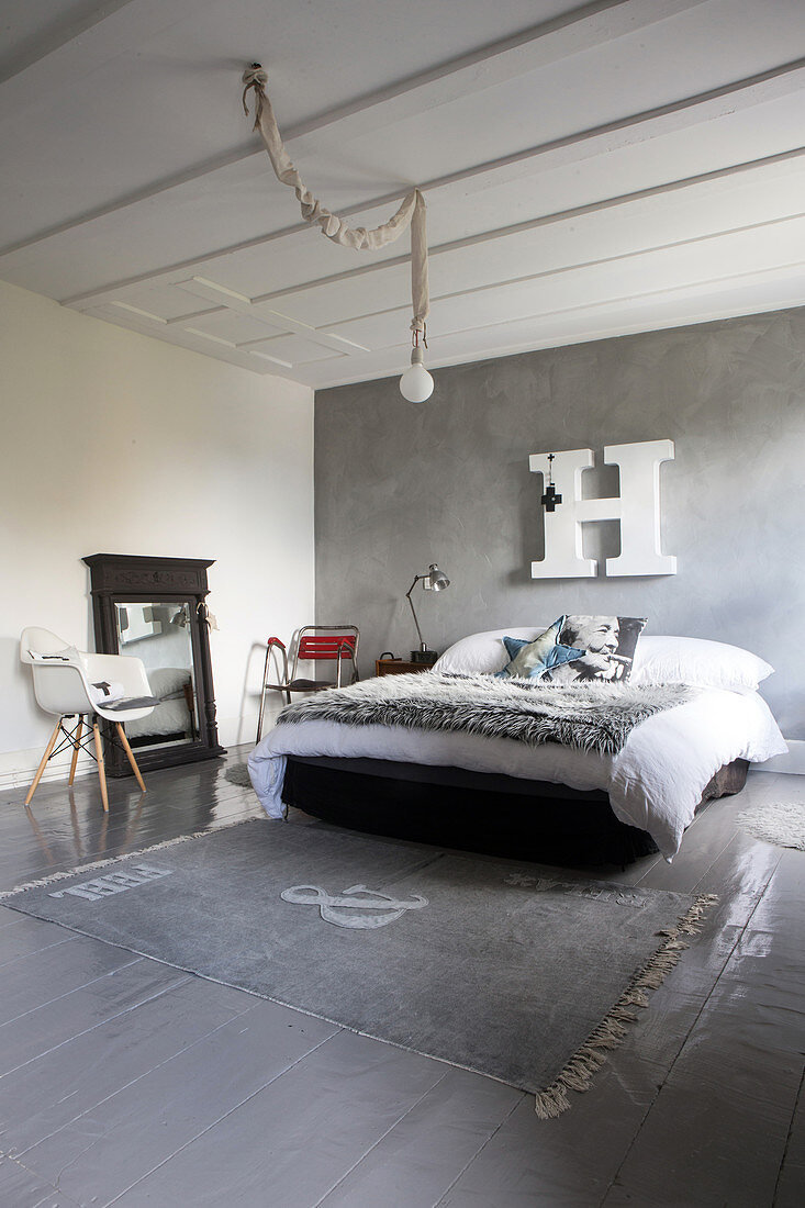 Fur blanket on bed below decorative letter on grey stucco lustro wall in bedroom with grey wooden floor and rug