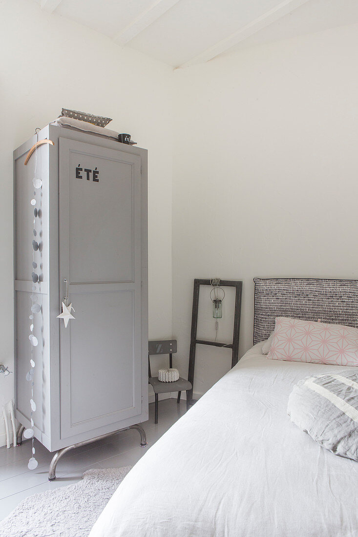 Blick über Bett auf grauen Schrank in schlichtem Schlafzimmer