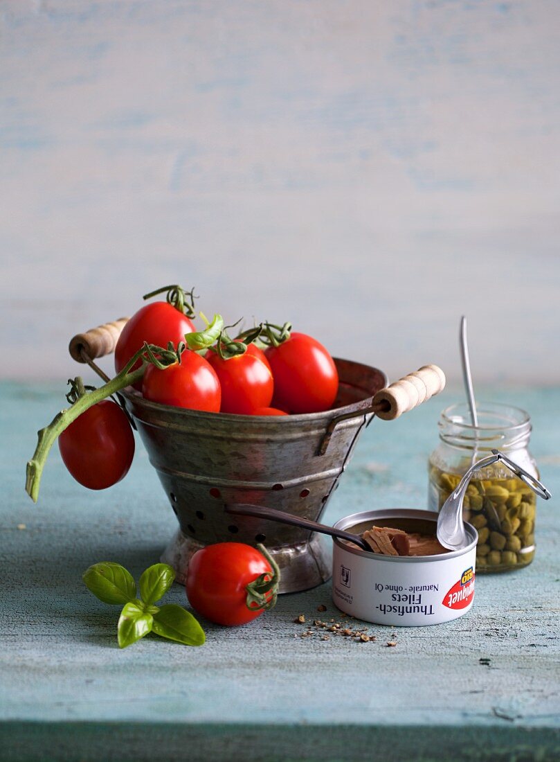 An arrangement of tomatoes, a tin of tuna fish, a jar of capers and basil