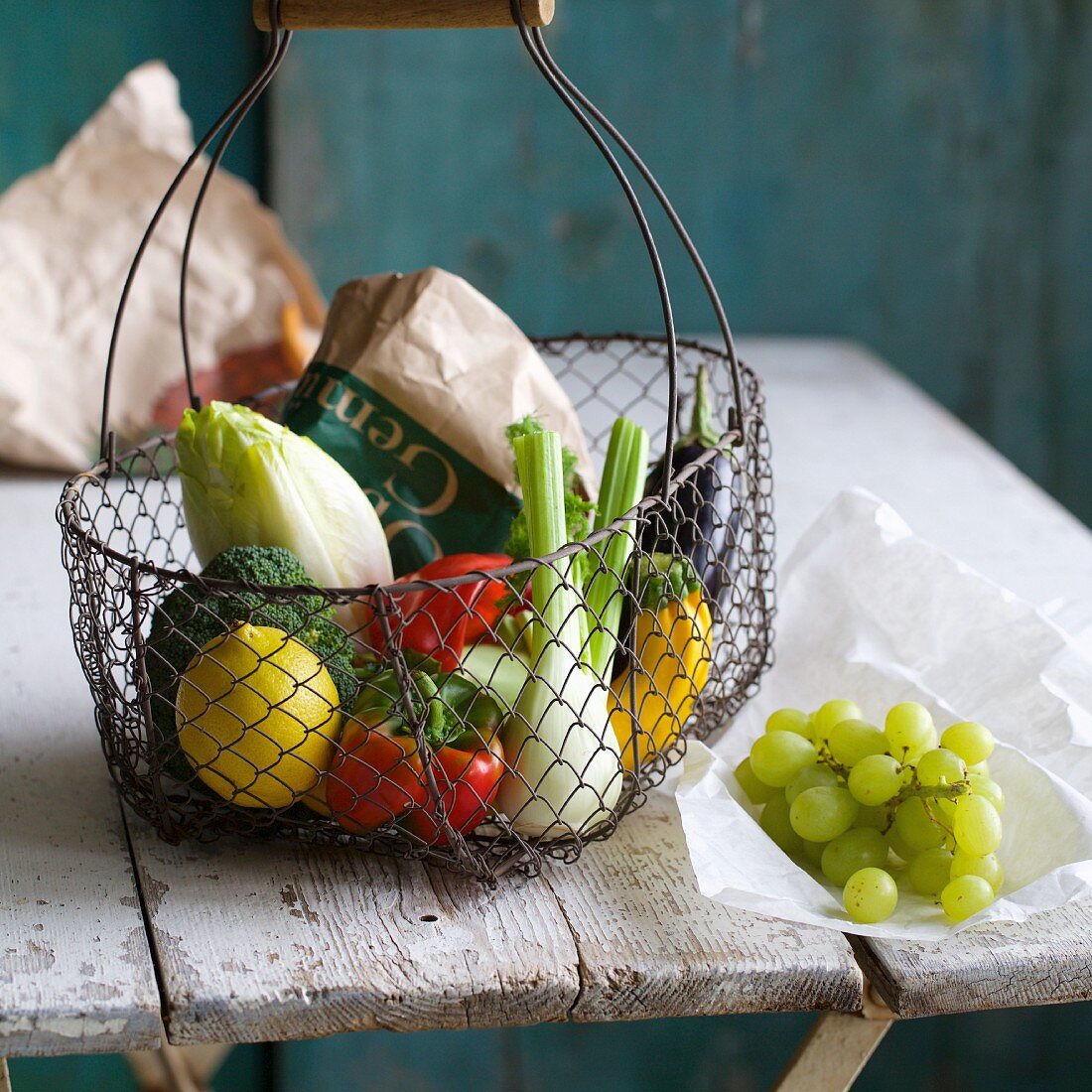 Einkaufskorb mit Gemüse und Zitrone, daneben Trauben auf altem Holztisch
