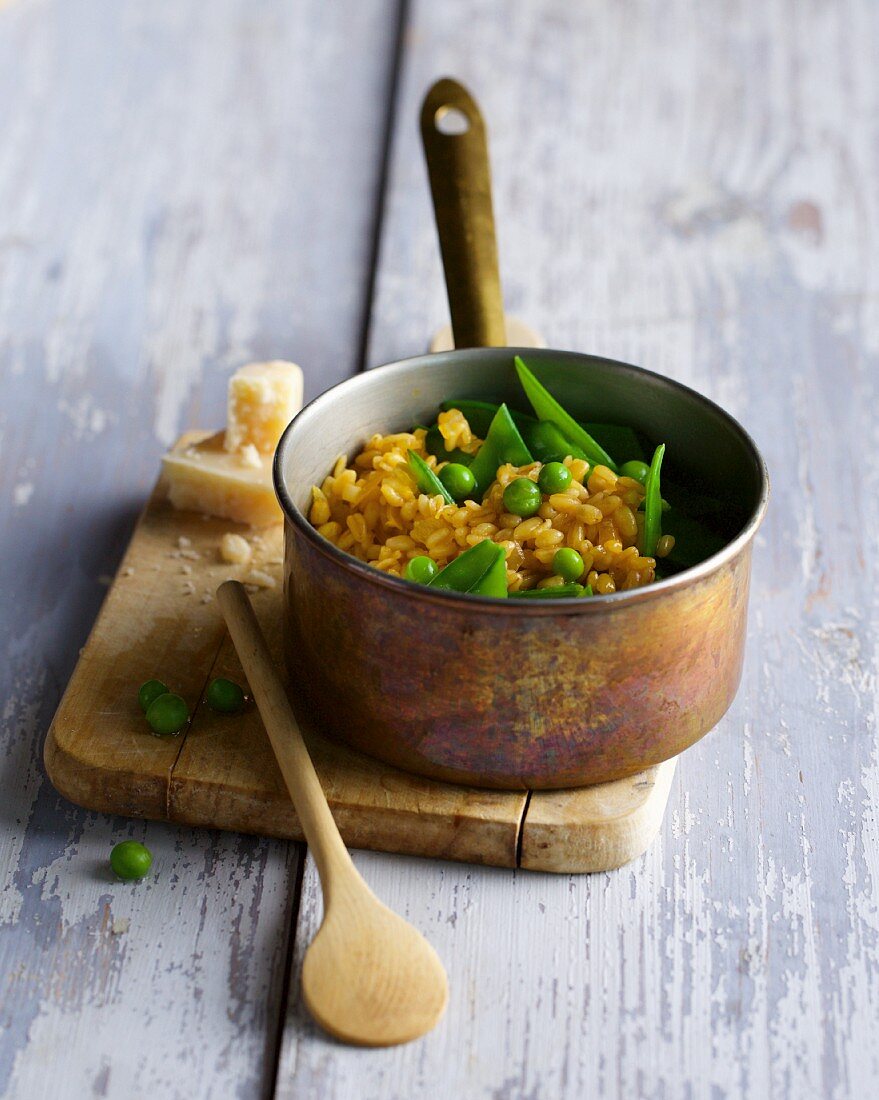 A copper saucepan with wheat risotto and peas