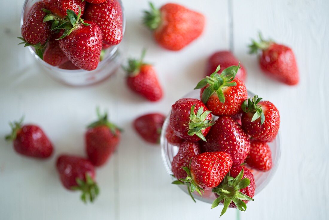 Freshly washed strawberries in glasses on a white wooden surface
