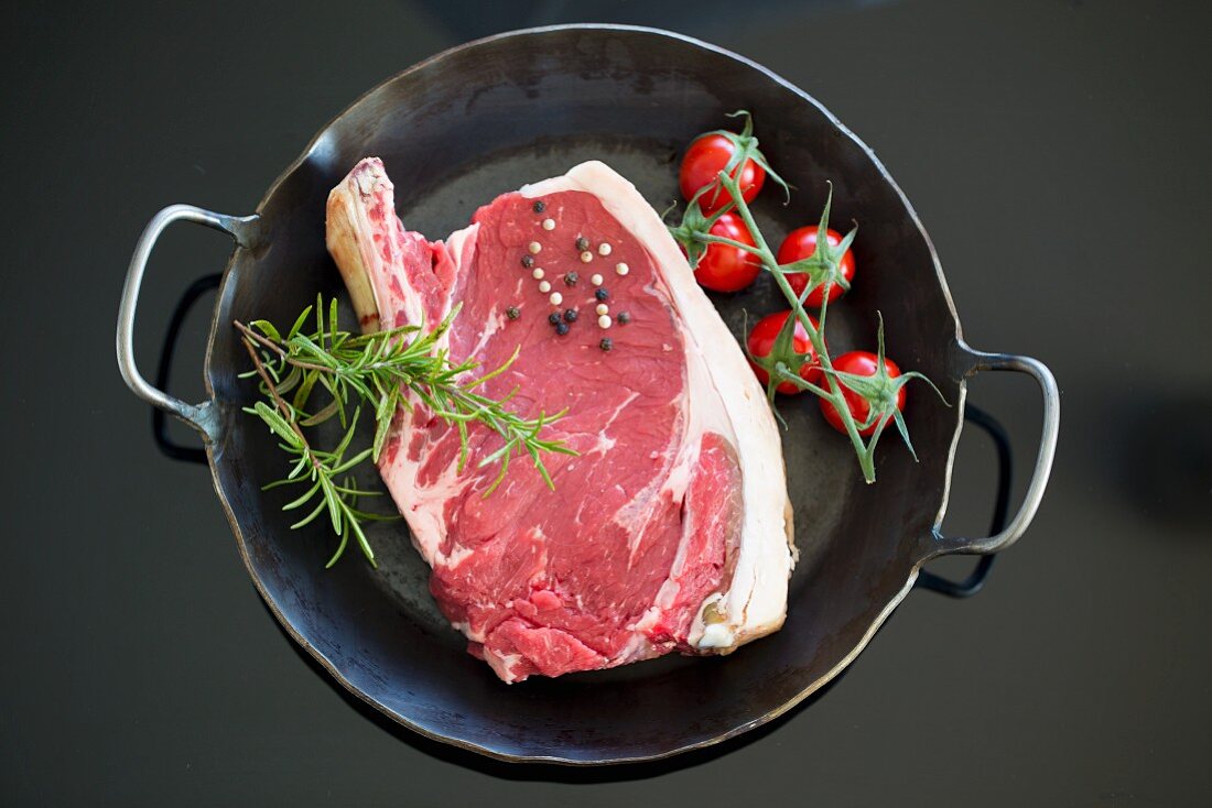 Cote de boeuf in a cast iron pan with tomatoes, rosemary and peppercorns